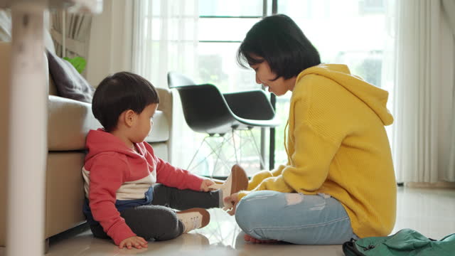 Asian mother helping her little son put on his shoes