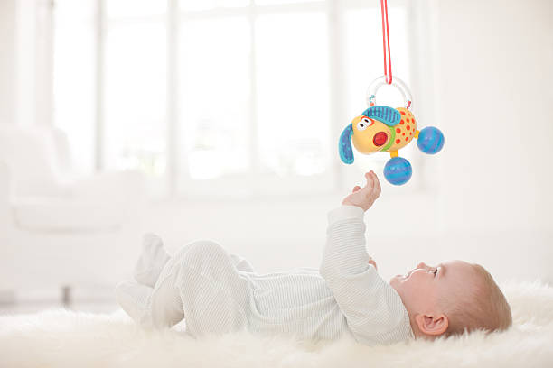 Baby on rug reaching for hanging toy overhead  hanging mobile stock pictures, royalty-free photos & images