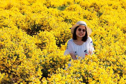 Asian woman wears white dress, happiness in yellow flower garden.