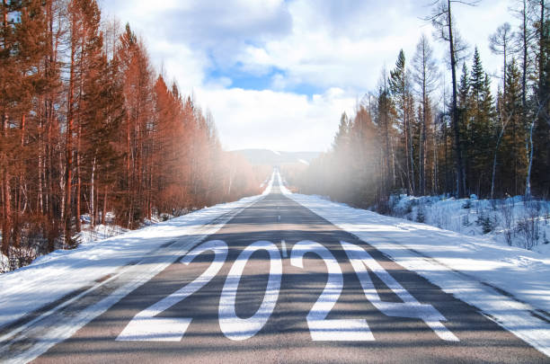 das wort 2024 steht auf der autobahn mitten auf einer leeren asphaltstraße im morgengrauen und einem wunderschönen blauen himmel. konzept für das neue jahr 2023. begriff - neujahrsvorsatz stock-fotos und bilder