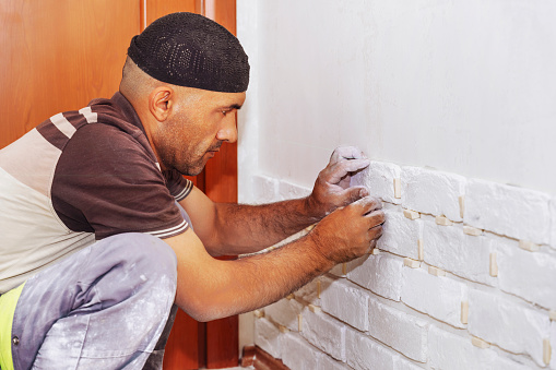 A man glues a white decorative stone in the form of a brick to the wall. Decor element, copy space for text,sticks decorative brick