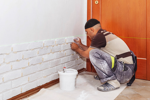 A man glues a white decorative stone in the form of a brick to the wall. Decor element, copy space for text,sticks decorative brick