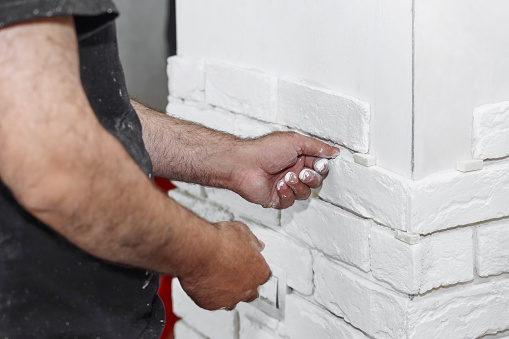 Man decorates the wall with decorative white torn bricks, close up view, DIY