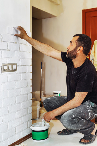 Tiler in the process of laying white rectangular brick tiles on bathroom wall. Stylish trendy white brick tile with a chamfer on the kitchen wall. Repair of apartments and bathrooms.