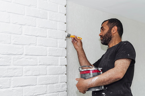 male hand painting white brick wall with paint brush