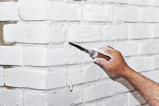 Plasterer using a finishing trowel to smooth new plaster on the surface of a white brick wall in a house interior during renovations or construction in a close up view