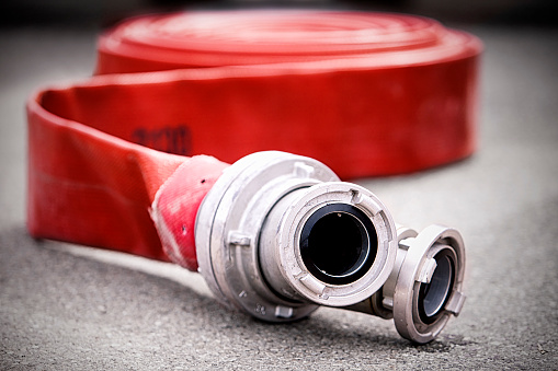 Red rolled up rubber firehose with metal nozzles