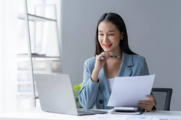 istock Beautiful young female manager or company worker holding accounting document, checking financial data or marketing report working in office with laptop. Accountant consults on some document. 1711011930