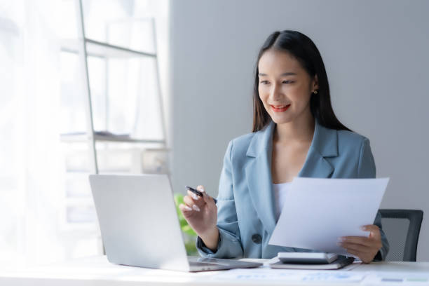 istock Beautiful young female manager or company worker holding accounting document, checking financial data or marketing report working in office with laptop. Accountant consults on some document. 1711011936