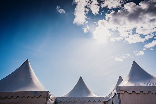 Peaks of three pyramidal white tents and blue sky background with space for advertisers text.