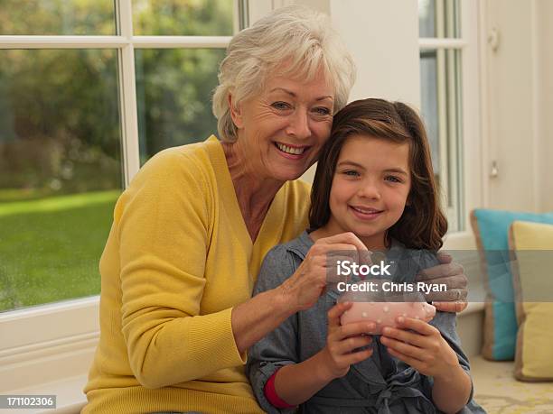Grandmother Putting Coin Into Granddaughters Piggy Bank Stock Photo - Download Image Now