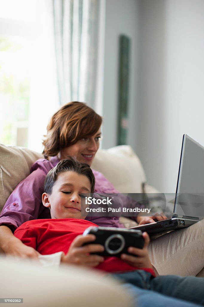 Madre utilizzando computer portatile e figlio, riproduzione video gioco - Foto stock royalty-free di Bambino