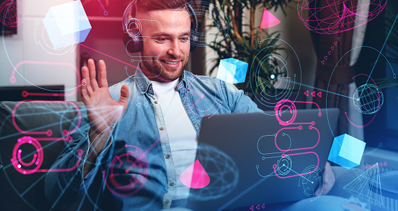 Happy businessman in headphones, waving hand looking at laptop, double exposure with metaverse icons and dashboard, blockchain and information fields. Concept of virtual meeting