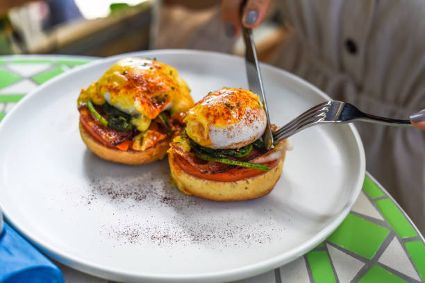 istock Hands with knife and fork cutting english muffin with poached eggs, bacon and Hollandaise sauce with vegetables 1711037451