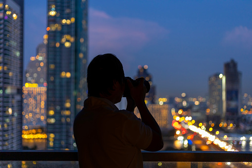 Photographer is taking cityscape photograph from the hotel balcony with evening street light at sunset scene for urban travel usage