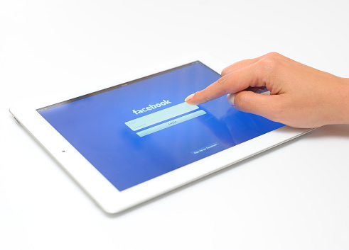 Astanbul, Turkey - May 18, 2012: Womans hand touching The New iPad displaying the start up screen of the Facebook Application. The third generation iPad is a touchscreen tablet pc produced by Apple Inc. The new iPad as known as iPad 3.