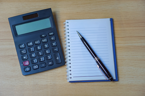 calculator with notebook and pen on wooden table