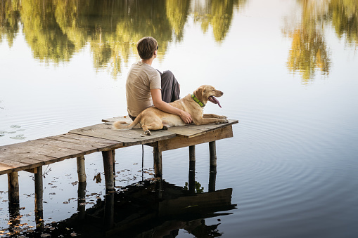 Female with a labrador dog on a wooden fishing bridge enjoying peaceful warm water view. Relaxatioan and spare time with home pets.