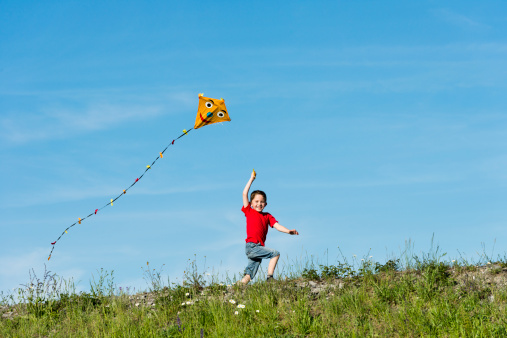 Close-up of a boy holding many kites in hand smiling over blue sky