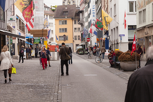Zurich, Switzerland - May 23, 2012: Street Scene in Zurich, Spring Afternoon. People are shopping on the Rennweg, a popular shopping street just off the famous Bahnhofstrasse in Zurich.  Slow Shutter.  Overcast weather after a light rain has fallen.  Pedestrian zone with colorful flags