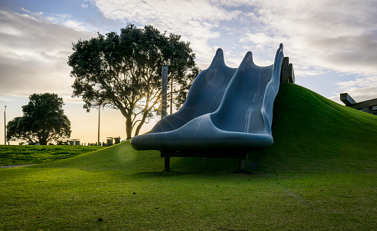 Empty playground slide and Pohutukawa tree at sunrise. Auckland.