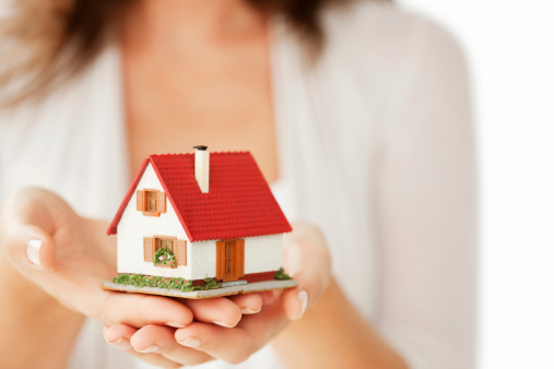 Close-up of woman's hands holding a small model house. Horizontal shot. Isolated on white.