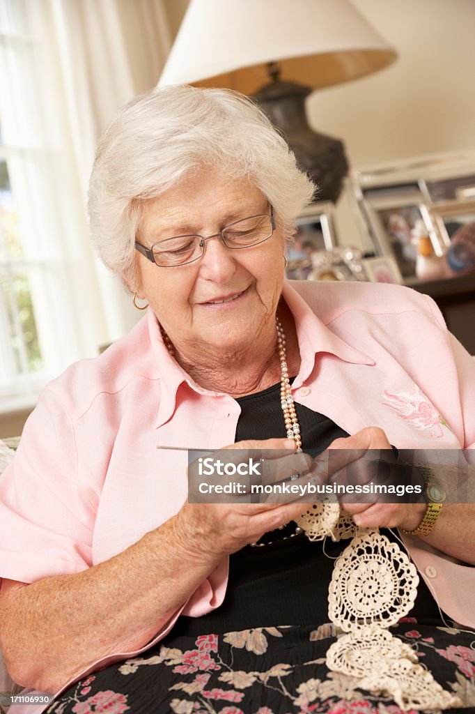 Retired Senior Woman Sitting On Sofa At Home Doing Crochet Retired Senior Woman Sitting On Sofa At Home Doing Crochet In Living Room. 70-79 Years Stock Photo