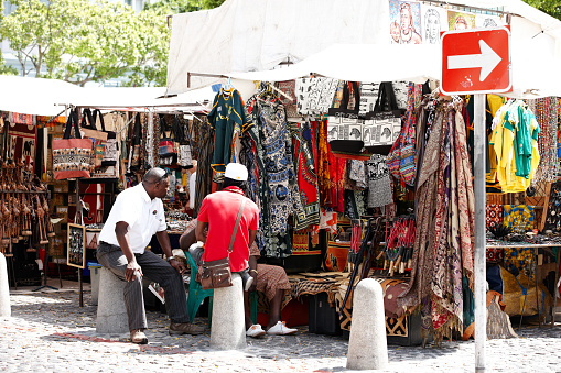 Cape Town, South Africa - January 31, 2012: Tourist shopping souvenirs on sale at a Cape Town market stall. Shop owners sit among their merchandise