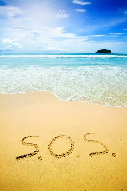 S.O.S. written on the sand of a beautiful tropical beach. Visible are footprints in the sand, one island in the sea, turquoise water, little splashy waves, golden sand and beautiful cloudscape over the sea.See more images like this in: