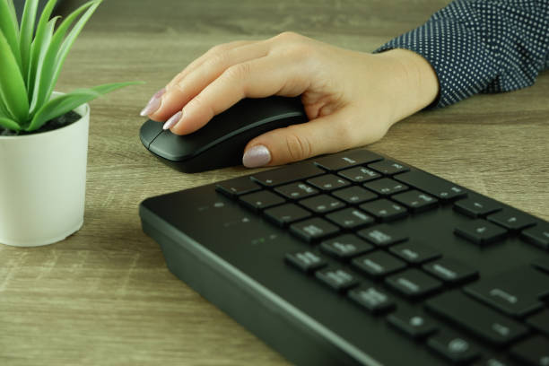 istock A woman's hand works with a mouse and keyboard manipulator. Caucasian Woman using a black wireless computer mouse on wooden background. Female hand with modern computer mouse 1711102910