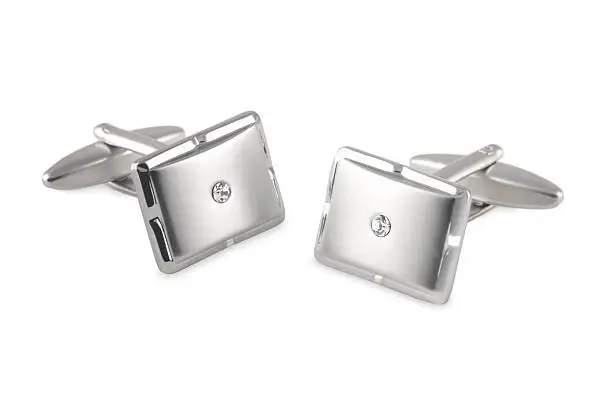 a pair of elegant men's cufflinks made from bright metal with brushed faces and a small white crystal inset. Taken against a white background.