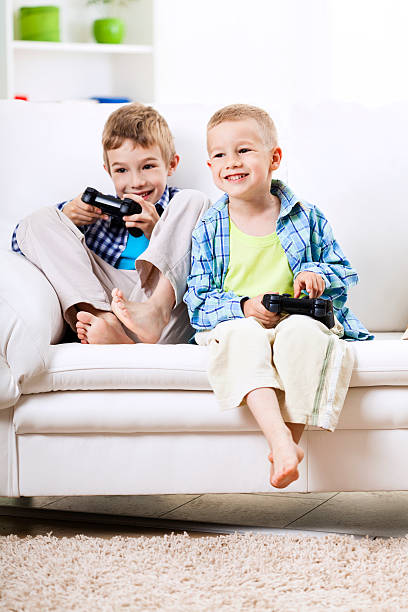 Two little boys playing video games at home, holding gamepads.