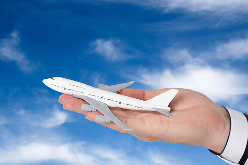 A man's hand holds a model of a passenger airliner against the background of a sky with clouds. Conceptual image.