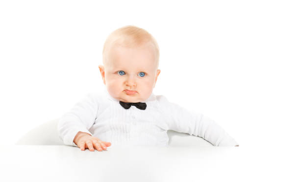 Disgusted elegant little boy looking at camera, leaning on the white table.More in