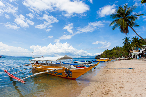 Sabang, Philippines - May 15, 2012: Outrigger boat moored on the beach on a clear day. A man is sitting in the back of the boat.