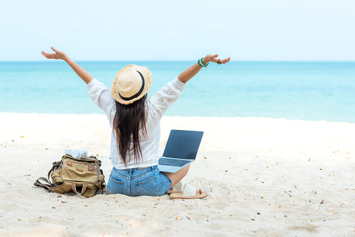 Lifestyle freelance woman raise arms relax after using laptop working on the beach.  Asian people success and together your work pastime and meeting conference on internet in holiday. Business and Summer Concept