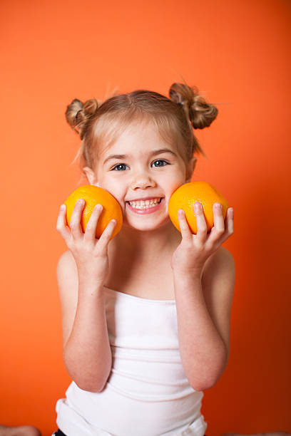Cute Little Girl with Oranges on Orange Background stock photo