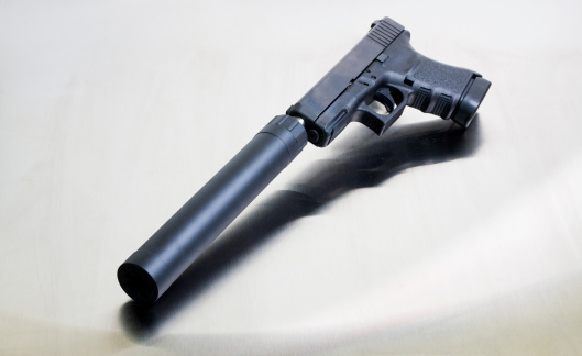 A modern black polymer (Glock) firearm with a suppressor attached on a stainless steel background.