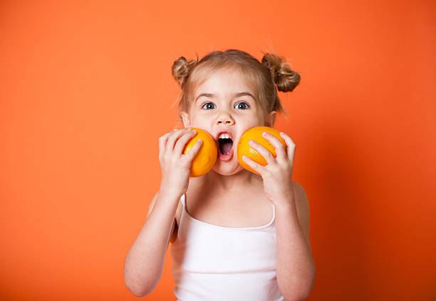 A little girl holding two oranges to her face stock photo