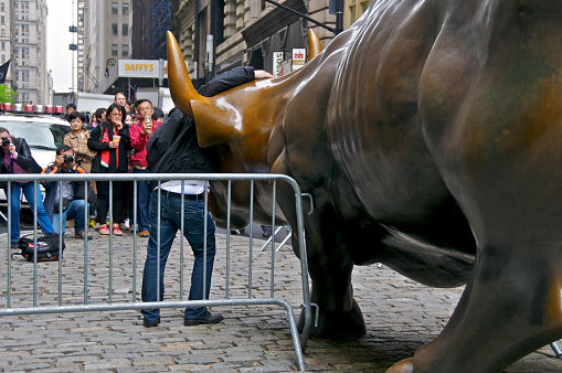 New York City, USA - May 09, 2012: Visiting Asian tourists are seen posing for photos standing near the NYPD protected Charging Bull, sometimes called the Wall Street Bull along Broadway at Bowling Green, Manhattan Financial District.