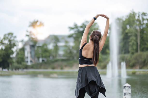 um retrato de uma jovem asiática esportiva e feliz em roupas esportivas está esticando os braços, aquecendo seu corpo antes de correr ao ar livre. conceito de atividade ao ar livre - aquecimento físico - fotografias e filmes do acervo