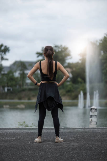 um retrato de uma jovem asiática esportiva e feliz em roupas esportivas está esticando os braços, aquecendo seu corpo antes de correr ao ar livre. conceito de atividade ao ar livre - aquecimento físico - fotografias e filmes do acervo