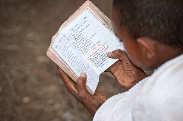 Novice in an orthodox monastery is reading a holy book Lalibela, Ethiopia - November 8, 2011: A novice of an orthodox monastery is sitting in the compound of the rock hewn churches of Lalibela in Northern Ethiopia and is reading a book written in the old language of the church, called Geez. ethiopian orthodox church stock pictures, royalty-free photos & images