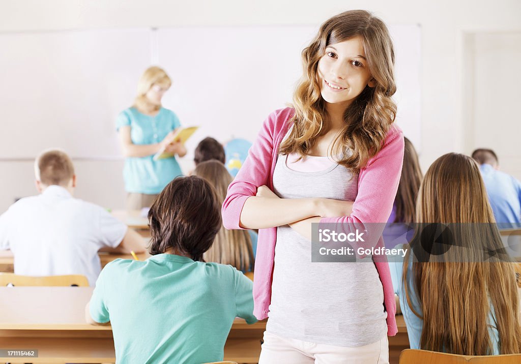Students in classroom, cheerful girl looking at camera Students in classroom, rear view, cheerful girl standing and  looking at camera. 10-11 Years Stock Photo