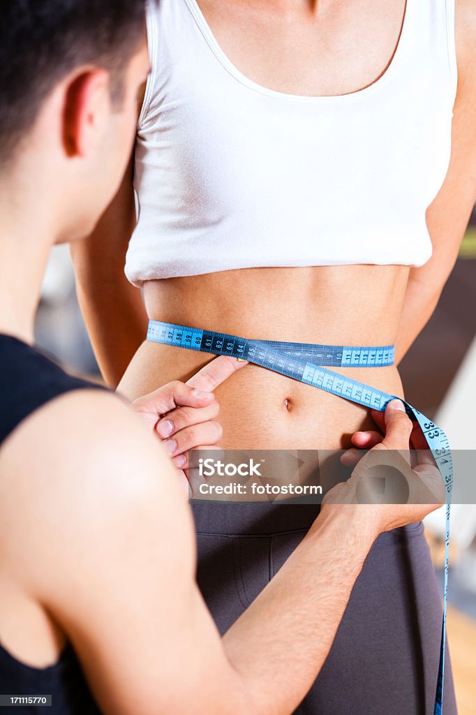 instructor de acondicionamiento físico de medición waistline de mujer en el gimnasio - Foto de stock de Abdomen libre de derechos