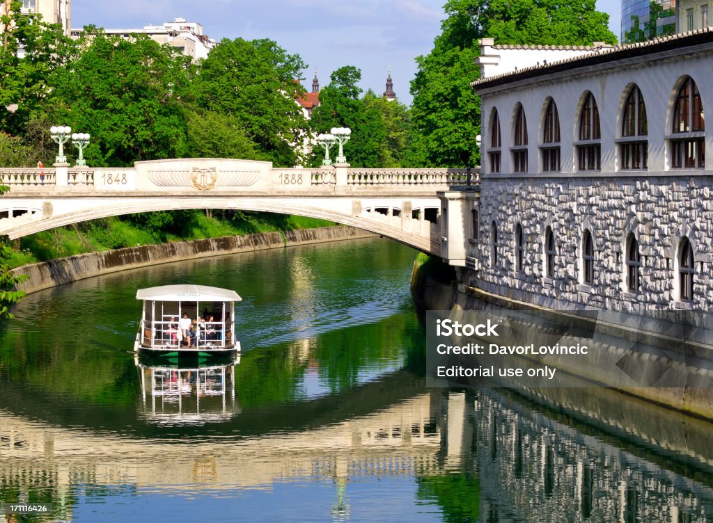 Boat and shadow Ljubljana, Slovenia - May 1, 2012: Triple bridge view of people on the boat with shadow under the bridge in center of Ljubljana. On right side is central open food market. Bridge - Built Structure Stock Photo