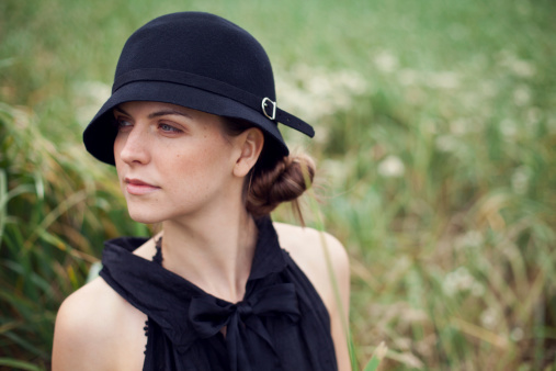 Young lady wearing 1920s vintage style cloche hat, standing in tall beach grass.