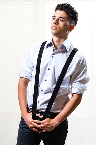 Handsome young man posing, wearing semi casual, modern clothing, pulling suspenders.