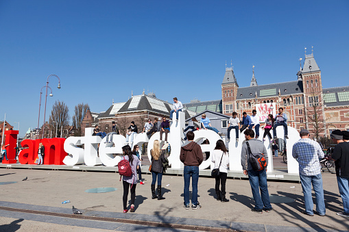 Amsterdam, the Netherlands - March 28, 2012: Young people posing on a part of the large public sculpture I Amsterdam letters in front of the Rijksmuseum at the Museumplein. Lots of people and tourists like to take pictures on top or in front of the letters.