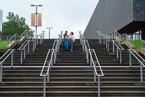 Women walking together holding an umbrella going down stairs